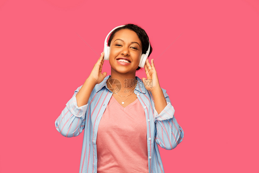 人,技术音频设备的快乐的非裔美国轻妇女耳机听音乐的粉红色背景非洲女人戴着耳机听音乐图片