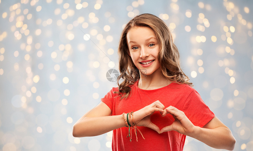 情人节,爱慈善理念微笑的十几岁女孩,留着长发,穿着红色T恤,节日的灯光背景下手势微笑的十几岁女孩穿着红色的手心图片