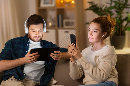 休闲,技术人的夫妇与平板电脑,耳机智能手机听音乐家里晚上家里听音乐的图片