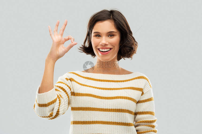 手势人的快乐的微笑轻妇女条纹套头衫手标志灰色背景快乐微笑的女人穿着条纹套衫,表现得很好图片