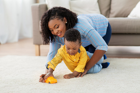 小孩玩具车童,孩子人的快乐的非裔美国母亲她的小儿子玩玩具汽车家里的沙发上妈妈宝宝家玩玩具车背景