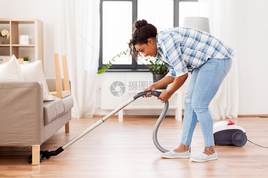 家庭家务快乐的非裔美国妇女家庭主妇与吸尘器清洁地板下的沙发家里家里吸尘器的女人家庭主妇图片
