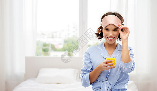 人们睡前的快乐的轻女人睡衣眼罩,着杯橙汁背景上女人睡衣带果汁的睡觉具图片