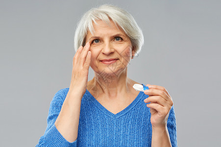 健康,视力老人的老妇女戴着灰色背景的隐形眼镜老妇女戴隐形眼镜图片