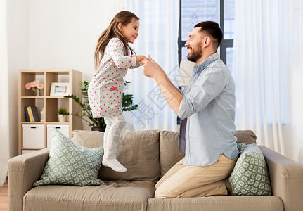 家庭,童父亲的快乐的父亲小女儿跳沙发上,家里玩得开心父亲女儿家里蹦蹦跳跳,玩得很开心背景图片