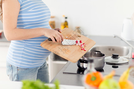 厨房小电怀孕,烹饪食物健康的饮食用菜刀孕妇,家里的炉子上加入切碎的粗糙的FTOM木砧板孕妇家烹饪食物背景