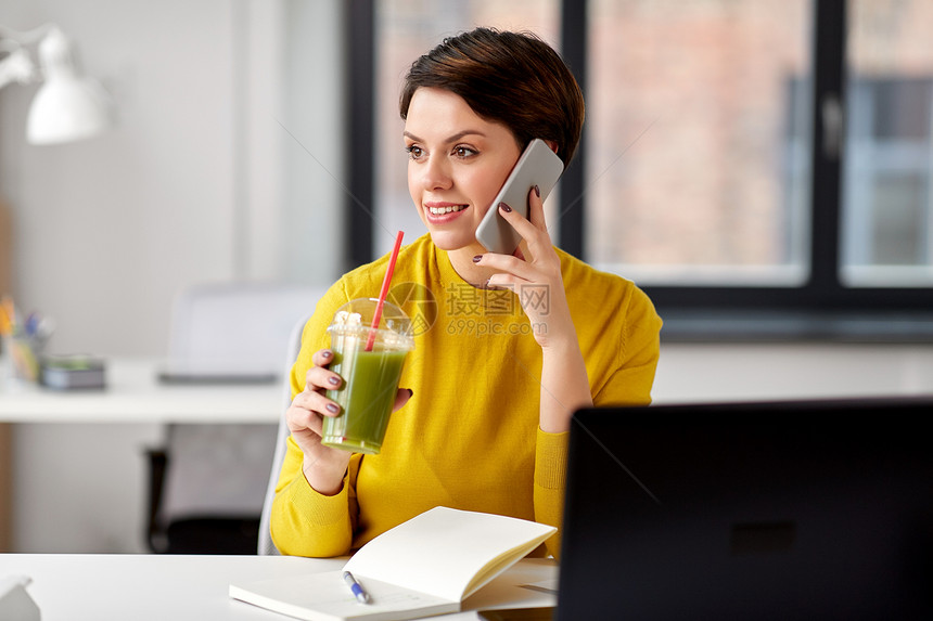 商业,技术人的女人喝奶昔打电话智能手机办公室饮料的女人办公室打电话给智能手机图片