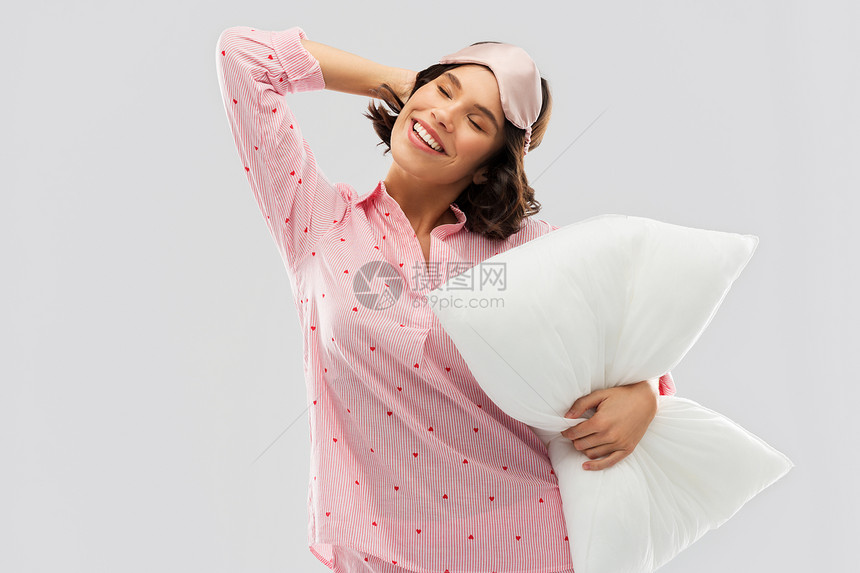 人们睡前的快乐的轻女人睡衣眼罩拥抱枕头伸展灰色的背景戴着睡衣枕头眼罩的女人图片