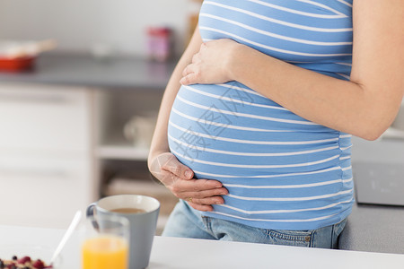 怀孕,生育期望密切孕妇触摸她的肚子家里厨房靠近孕妇抚摸她的腹部图片