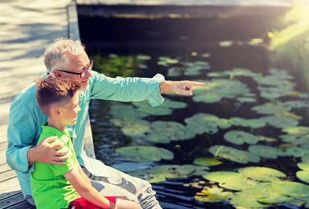 家庭世代交流人的快乐的祖父孙子坐河边祖父孙子坐河泊上图片