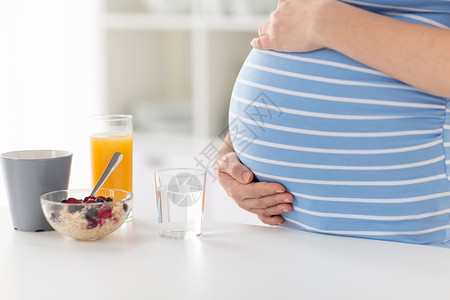 厨房果汁孕妇抚摸她的孕肚在厨房健康早餐背景