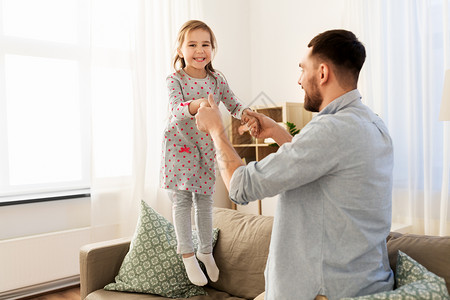 家庭,童父亲的快乐的父亲小女儿跳沙发上,家里玩得开心父亲女儿家里蹦蹦跳跳,玩得很开心背景图片