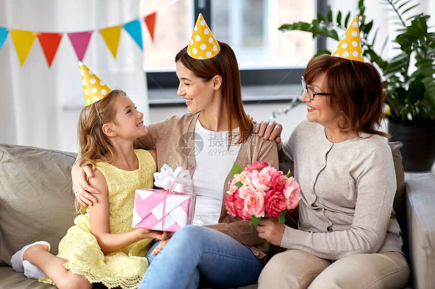 家庭世代庆祝微笑的女儿带着礼品盒,祖母带着鲜花家里迎接母亲的生日女儿带着礼品盒生日那天问候母亲图片