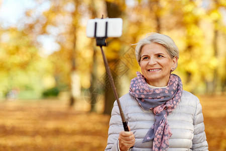 老退休技术快乐的老妇女秋季公园自拍杆拍照高级女人秋天公园自拍图片