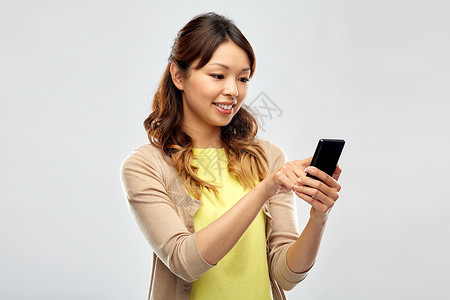 技术人的快乐的亚洲妇女用智能手机灰色背景用智能手机的快乐亚洲女人图片