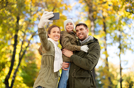 养育子女照片家庭休闲人的快乐的母亲父亲小女儿秋季公园背景下用智能手机自拍家人秋天公园用智能手机自拍背景