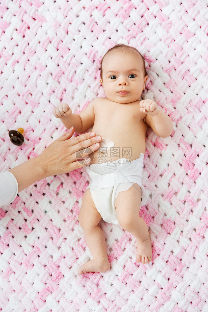 婴儿期,母亲人的母亲的手应用身体乳液,甜蜜的小女儿奶嘴躺针粉红色毛毯的毛绒纱手涂沐浴露女婴的肚子上图片