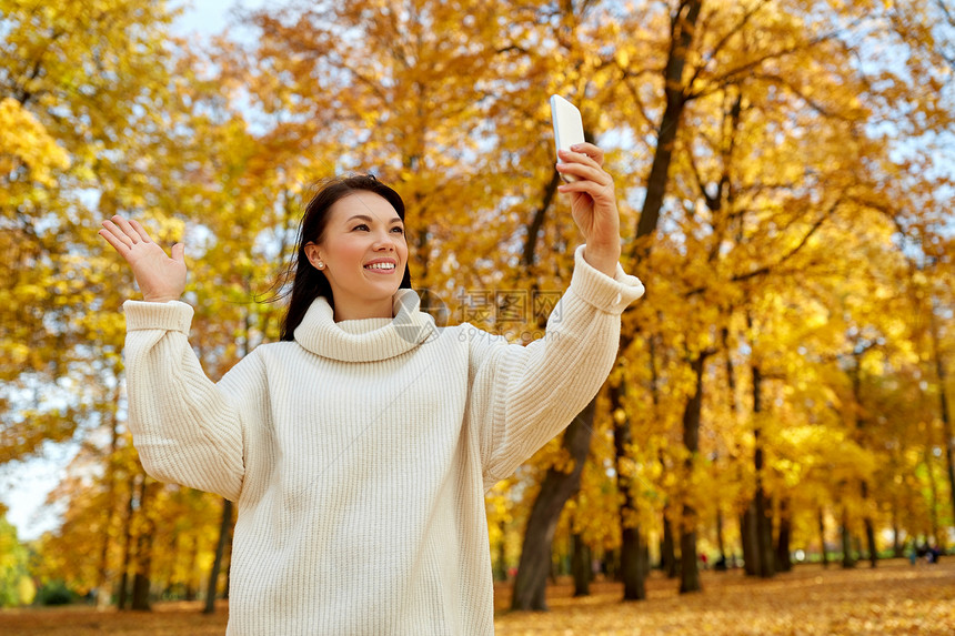 季节,技术人的美丽的快乐女人自拍秋季公园的智能手机上打视频电话女人秋天公园用智能手机自拍图片