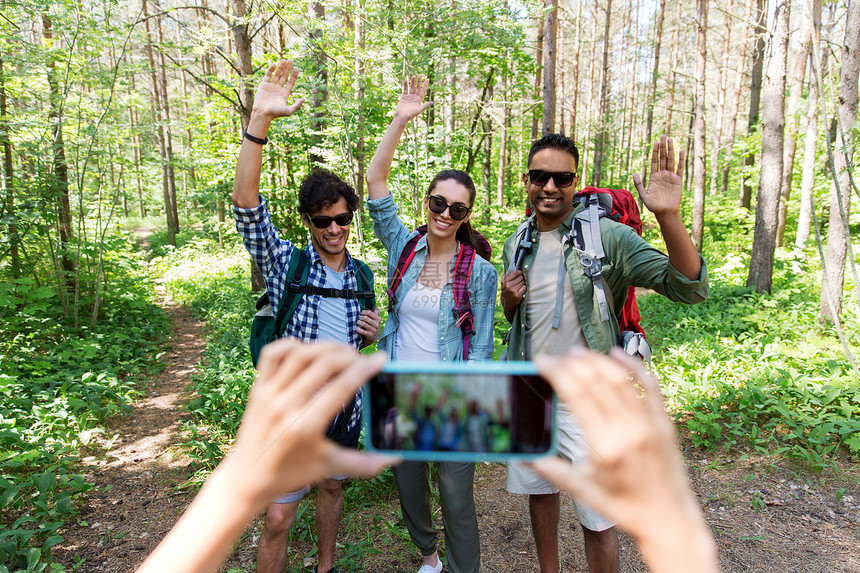 旅行,旅游徒步旅行的群朋友,背包挥舞着手,森林里被智能手机拍照带背包的朋友徒步旅行中被拍照图片