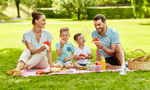 小朋宇吃西瓜家庭休闲人的快乐的母亲,父亲两个小儿子夏天的公园野餐吃西瓜快乐的家庭夏天的公园野餐背景