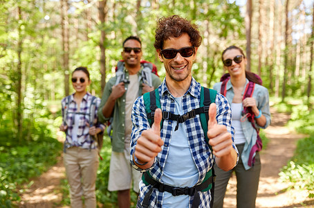 旅行,旅游,徒步旅行人们的群朋友带着背包男人森林里竖大拇指的手势背包的朋友森林里竖大拇指背景图片