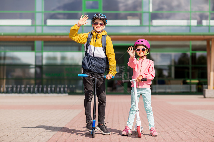 教育,童人的快乐的学校孩子戴着头盔,背包骑着滑板车,户外挥手快乐的学校孩子戴着头盔骑滑板车图片