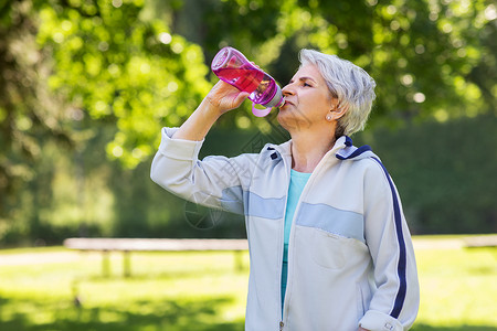 健身,运动健康的生活方式口渴的老妇女公园锻炼后瓶子里喝水老年女子公园锻炼后喝水背景图片
