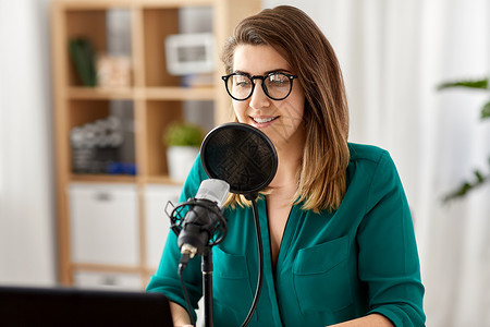 技术,大众媒体人们的戴着麦克风笔记本电脑的眼镜的女人录音室交谈录制播客演播室里麦克风录音播客的女人室内高清图片素材