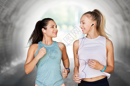 健身,运动健康的生活方式微笑的轻妇女女朋友与耳机运行户外耳机运行的女女朋友背景图片