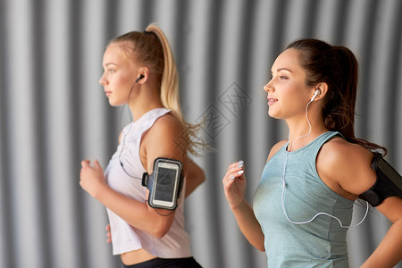 跑步耳机健身运动健康的生活方式轻女女朋友戴着带智能手机的,户外跑步带着耳机智能手机的轻女跑步背景
