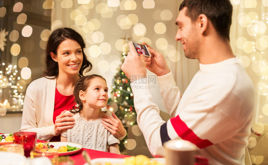 节日,家庭庆祝快乐的母亲,父亲小女儿吃诞晚餐,并家里用智能手机拍照快乐的家人诞晚餐上拍照图片