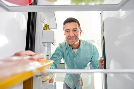 食物饮食饮食微笑的中男子厨房的冰箱里肉男人厨房的冰箱里食物包图片
