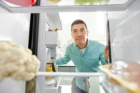 饮食饮食微笑的中男子厨房的冰箱里寻找食物厨房冰箱里找食物的人图片