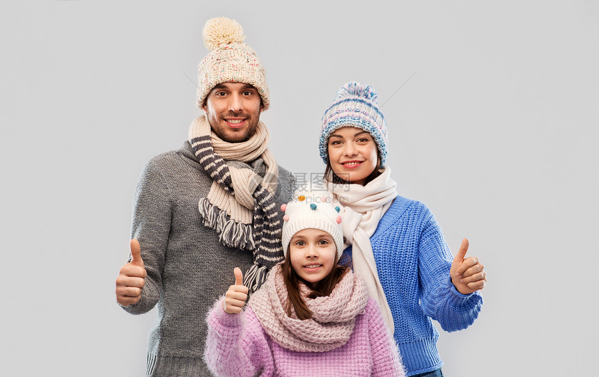 家庭,诞节冬天的衣服快乐的母亲,父亲小女儿戴着针帽围巾,灰色的背景上竖大拇指灰色背景下穿着冬天衣服的幸福图片