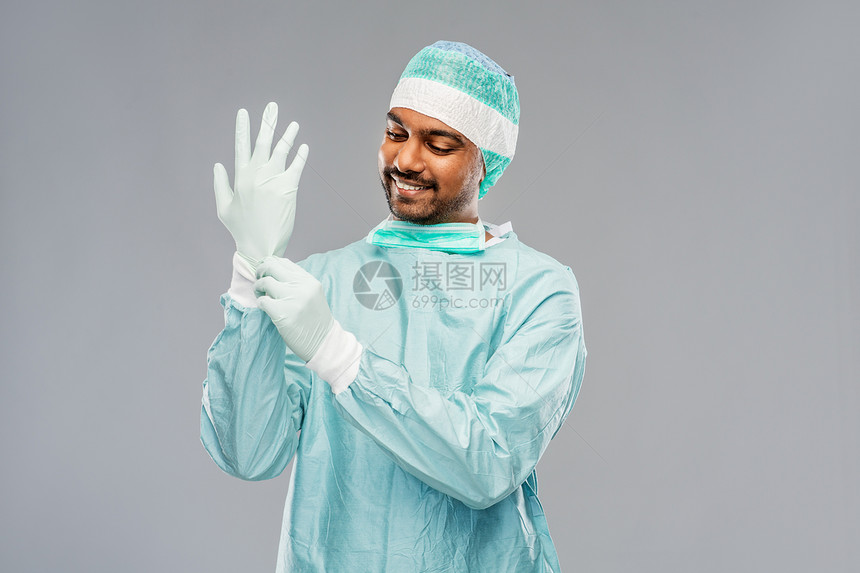 医学,外科人的微笑的印度男医生外科医生穿着防护服,戴着灰色背景的手套印度男医生外科医生戴上手套图片