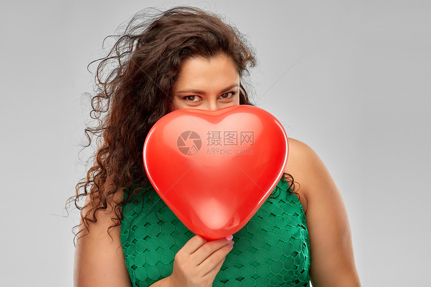 情人节,人与爱的嬉戏的女人穿着绿色的衣服躲红色的心形气球后灰色的背景顽皮的女人着红色的心形气球图片