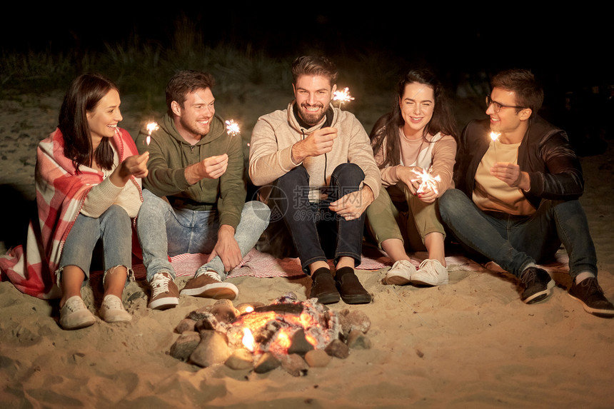 庆祝,假日人们的快乐的朋友与火花坐营地火海滩上的夜晚快乐的朋友与火花营地火灾晚上图片