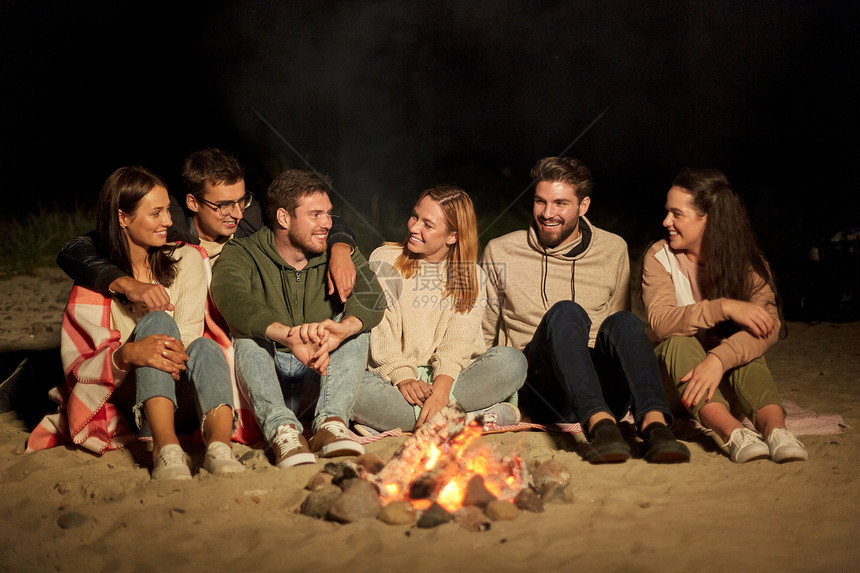 休闲人的群微笑的朋友晚上坐海滩上的篝火旁群朋友坐海滩上的篝火旁图片