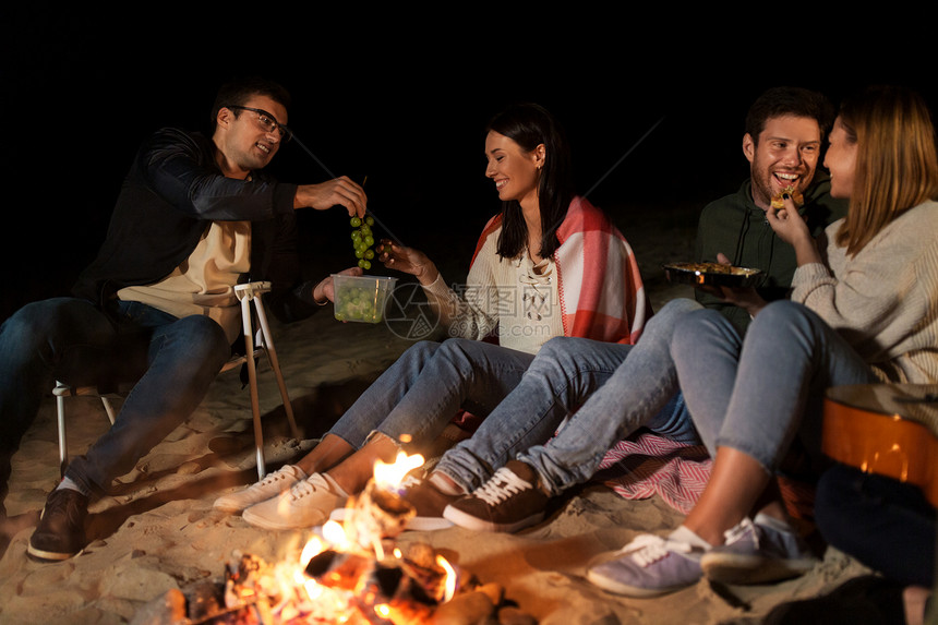 休闲人们的群微笑的朋友晚上海滩上的篝火上野餐朋友们海滩的篝火上野餐图片