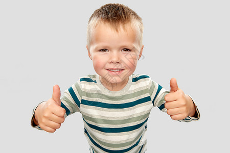 童,手势人的微笑的小男孩穿着条纹衬衫,灰色背景上竖大拇指穿着条纹衬衫的微笑男孩竖大拇指背景图片