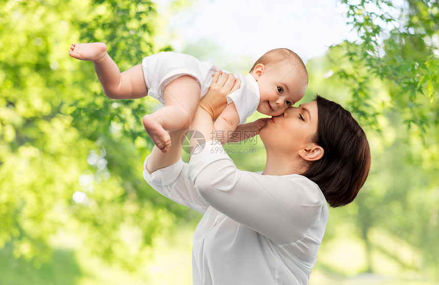 家庭,孩子父母的快乐的微笑中母亲亲吻小婴儿女儿的绿色自然背景快乐的母亲亲吻小宝贝女儿图片