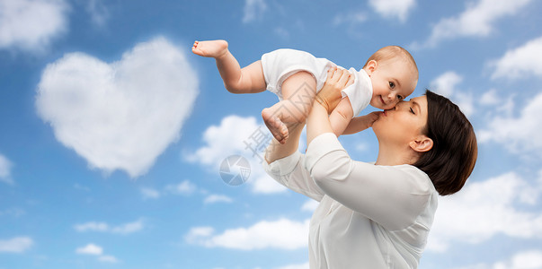 蓝天心形云背景下快乐的母亲亲吻小宝贝女儿背景图片