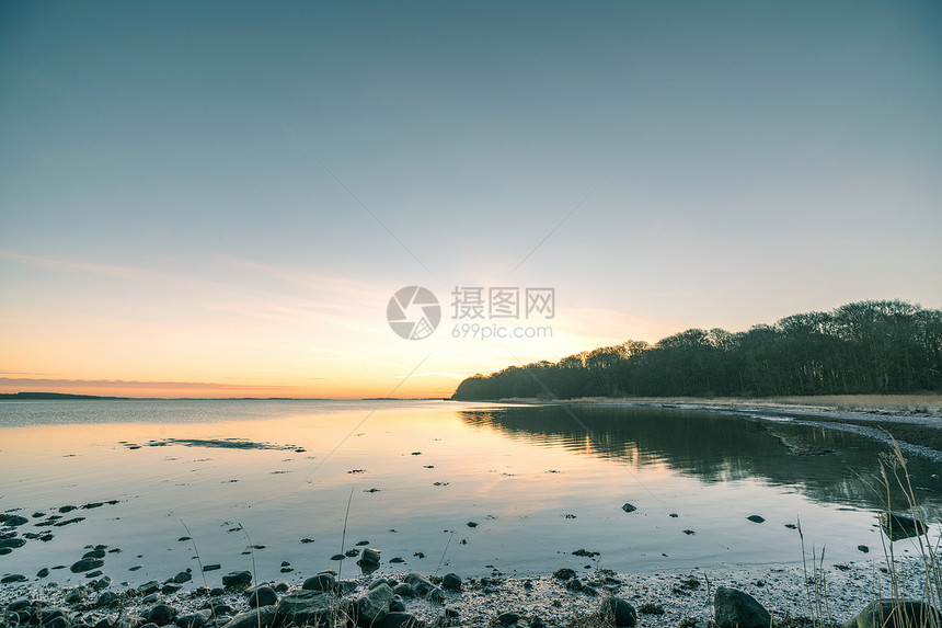 日出时的湖,海滩上岩石,岸边片森林图片