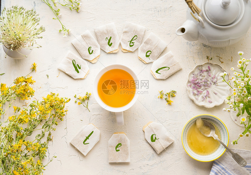 白色杯子与框架茶袋文字草药茶白色桌子背景,顶部视图带茶壶蜂蜜新鲜草药鲜花的草药茶具健康预防饮料治疗图片