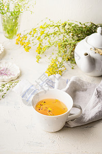 白色桌子上的杯草药茶,茶壶新鲜的草药鲜花促进免疫消化系统健康的自然疗法背景图片