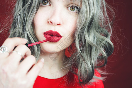 轻的女人用红色的哑光口红给她的嘴唇化妆图片