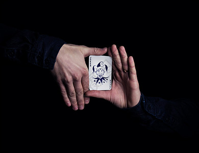 手的魔术素材双手紧握小丑扑克牌魔术师黑色背景上用卡片展示他的把戏背景