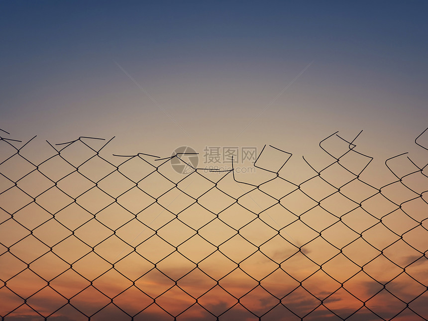 旧的铁丝网栅栏纹理在日落的天空背景下图片