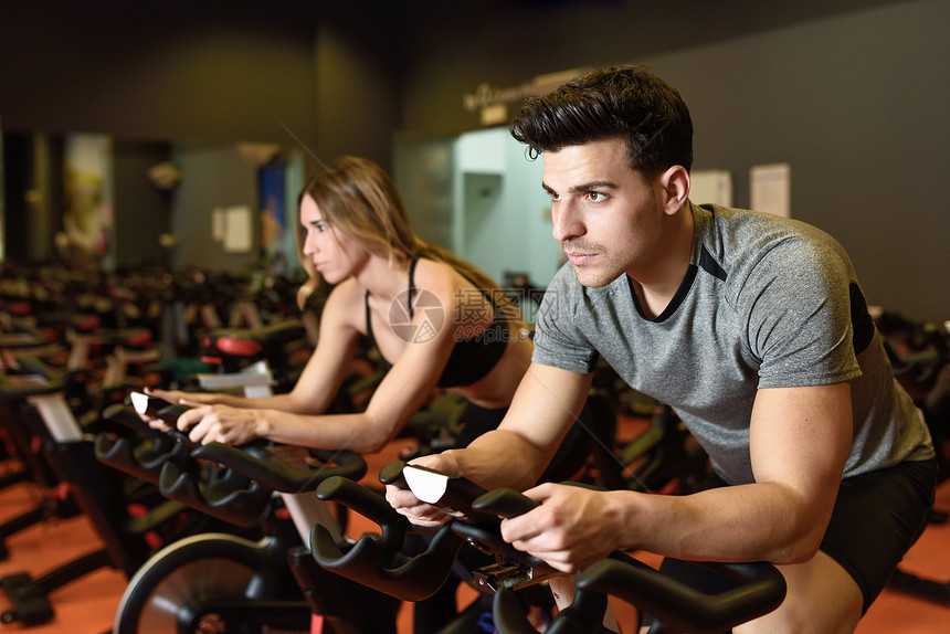 吸引力的女人男人健身房骑自行车,锻炼腿氧运动骑自行车夫妇课上穿着运动服图片