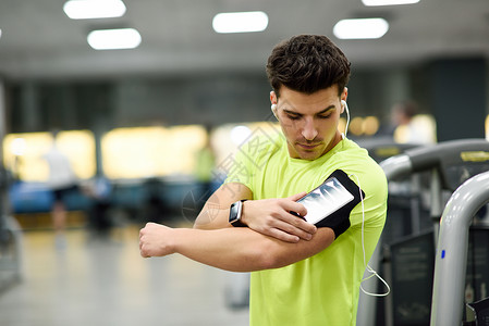 轻人用智能手机站健身房训练前迷人的男与智能手表图片